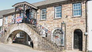A stone building with a covered staircase and a flag display. - The Snug (Dulverton)