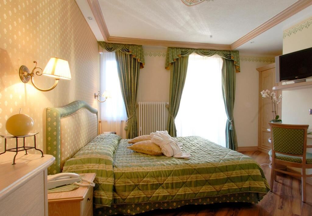 A hotel room with a bed, a bedside lamp, a telephone, and a television on a wooden cabinet.