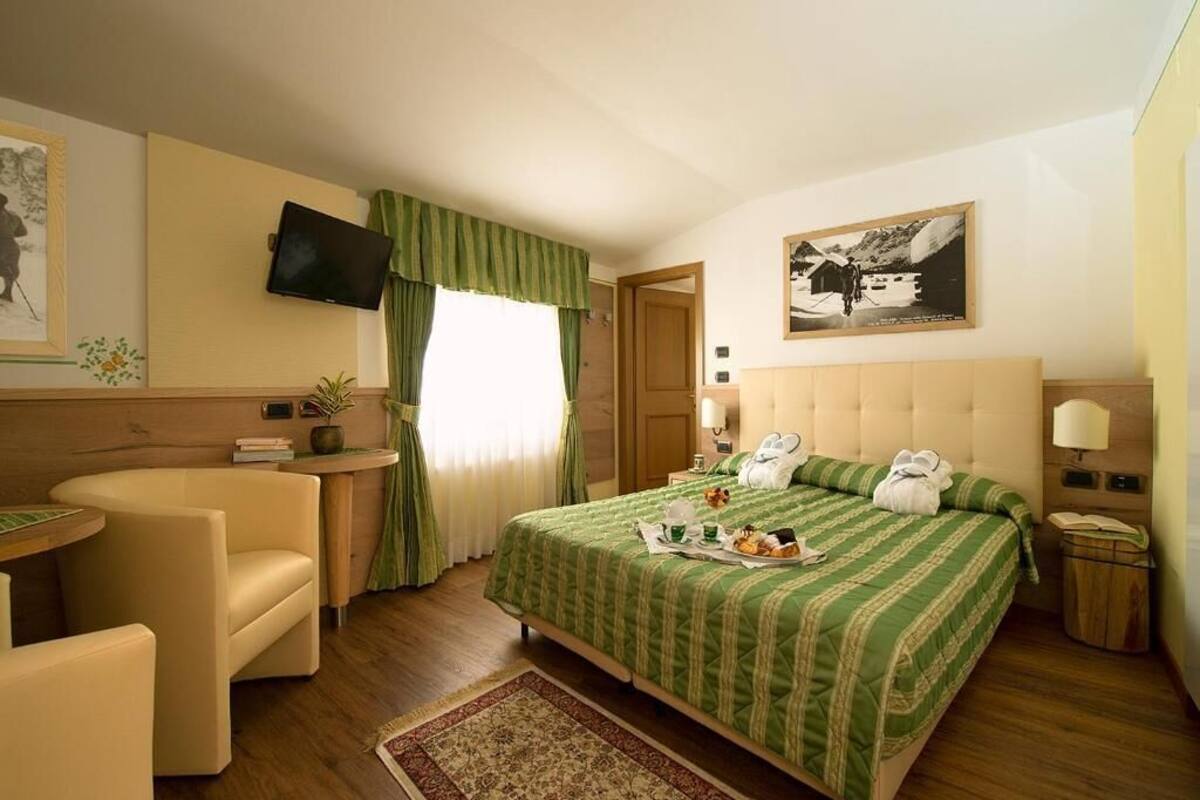 A hotel room with a bed, a desk, a chair, a TV, and a painting on the wall.