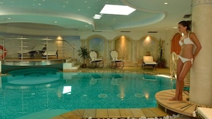 An indoor swimming pool with a diving board, lounge chairs, and a staircase leading to a higher level. - Hotel Alle Alpi (Moena)