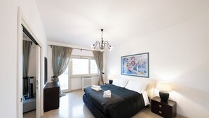 Et moderne hotelværelse med en stor seng, et sengebord med lampe, et vindue med gardiner og et billede på væggen.