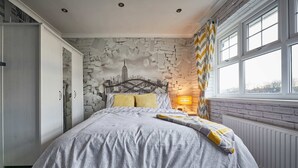 A bedroom with a bed, a cityscape mural, a radiator, and a window with curtains. - Host Stay Stonehaven (Hartlepool)