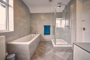 A modern bathroom with a bathtub, shower, and herringbone-patterned floor. - Host Stay Silverlinings (Whitley Bay)