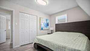 A bedroom with a bed, a nightstand, a lamp, a painting, and a window with blinds. - Full House- 2 Blocks from Beach! (Brigantine)