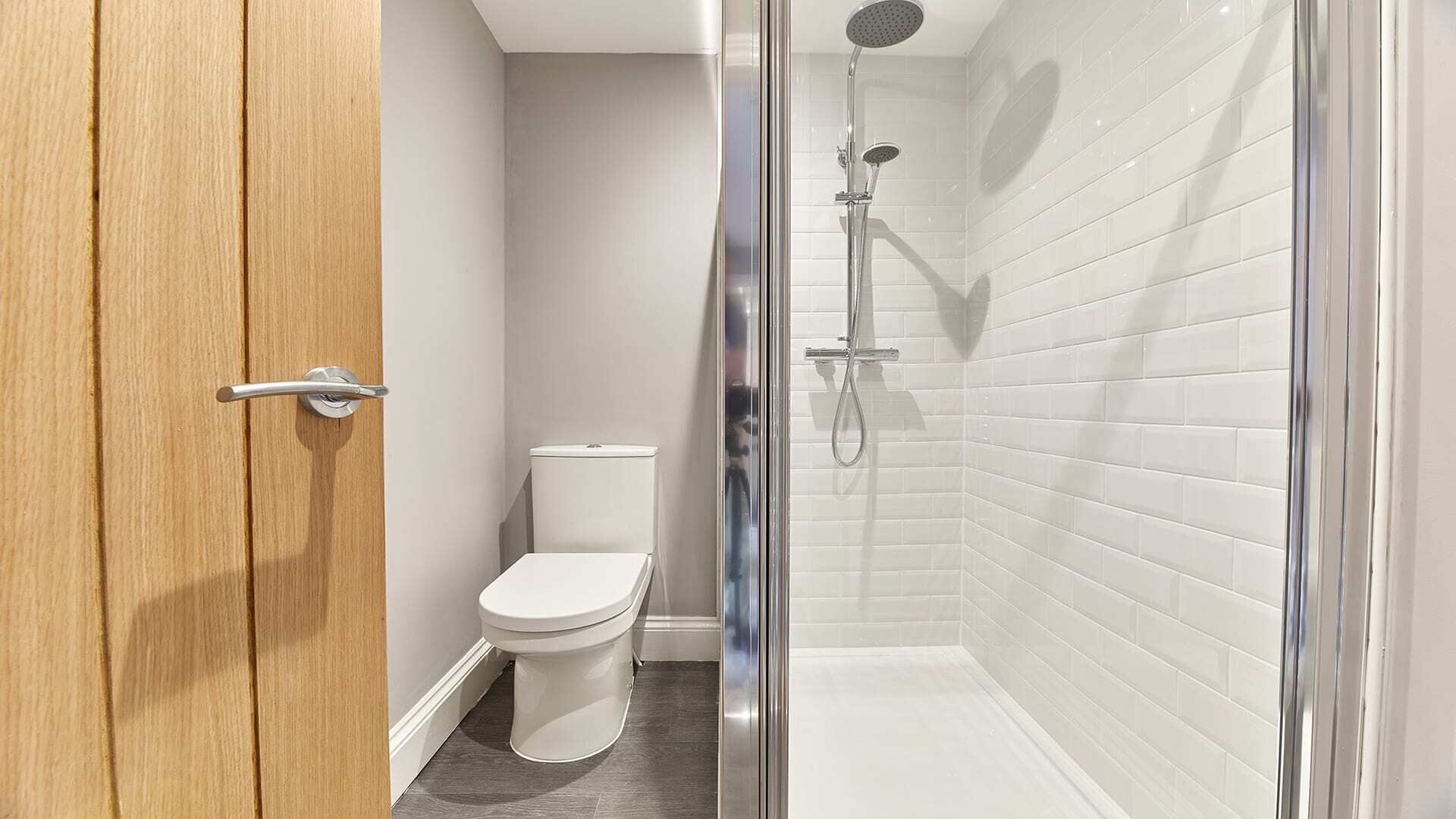 A modern bathroom with a glass shower enclosure, a toilet, and a wooden door.