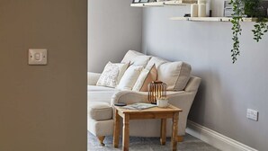 Ein gemütliches Wohnzimmer mit einem beigen Sofa, einem Holztisch und einer hängenden Pflanze.