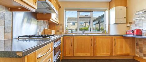 A modern kitchen with wooden cabinets, a gas stove, and a window with a view of the neighborhood.