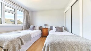 A bedroom with two single beds, a nightstand, and a window with curtains. - Host Stay Shorty s (Morpeth)