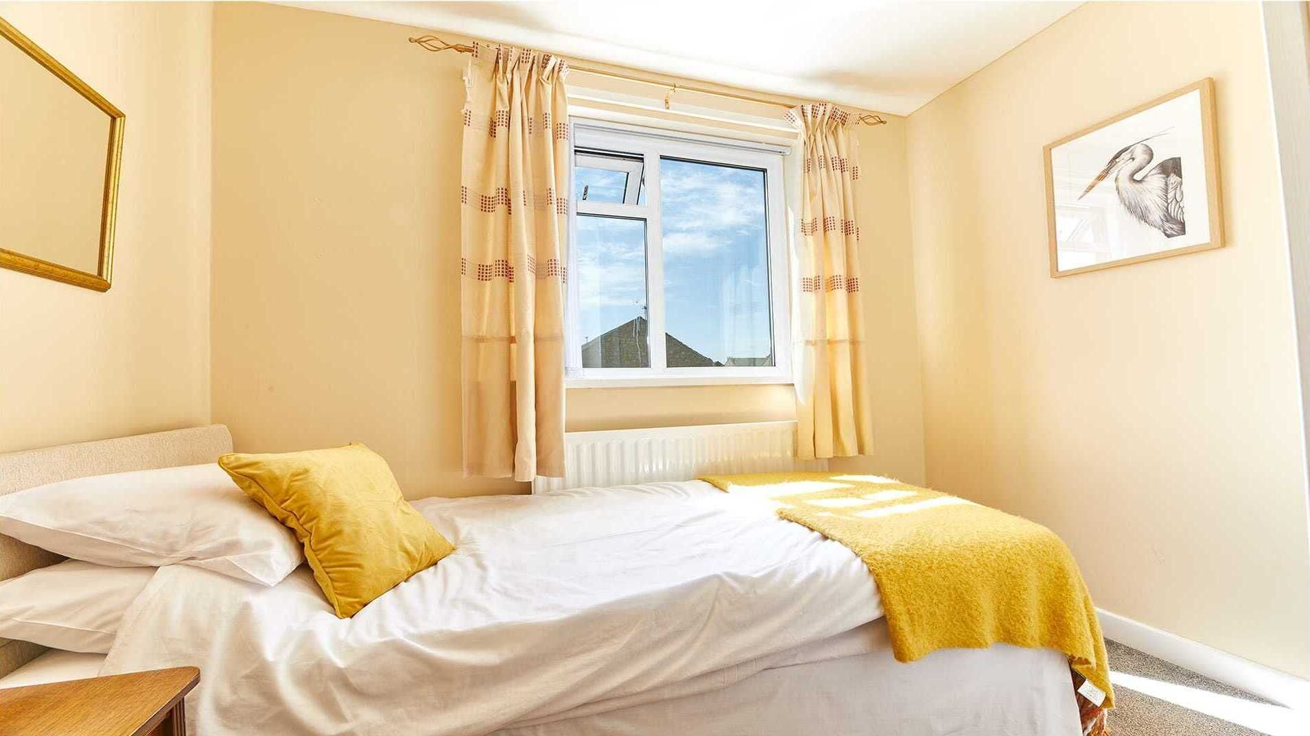 Un dormitorio con cama, una ventana con cortinas, un radiador y un cuadro en la pared.