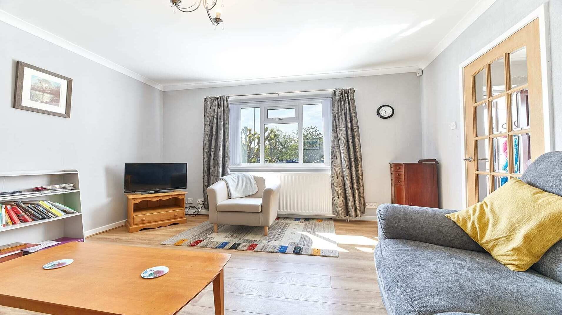 A living room with a sofa, a television on a wooden stand, a bookshelf, and a window with curtains.