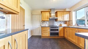 A modern kitchen with wooden cabinets, a gas stove, an oven, and a window providing natural light. - Host Stay Shorty s (Morpeth)