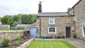Une maison en pierre avec un petit jardin, une porte bleue et une enseigne sur laquelle on peut lire « Chez Maggie ».