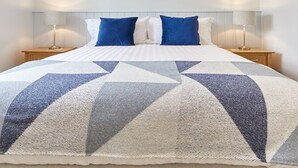 Une chambre à coucher moderne avec un grand lit, deux oreillers bleus, du linge de lit blanc et deux tables de chevet avec des lampes.
