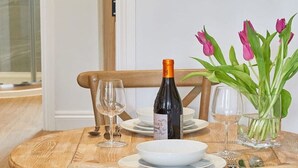 Une table de salle à manger en bois, avec une bouteille de vin, deux verres, une assiette et un vase de tulipes.