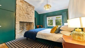 A bedroom with a stone fireplace, a bed with multiple pillows, a patterned rug, and a lamp on a bedside table.