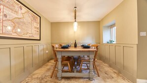 A dining area with a wooden table set for four, a map on the wall, and a window with plants.