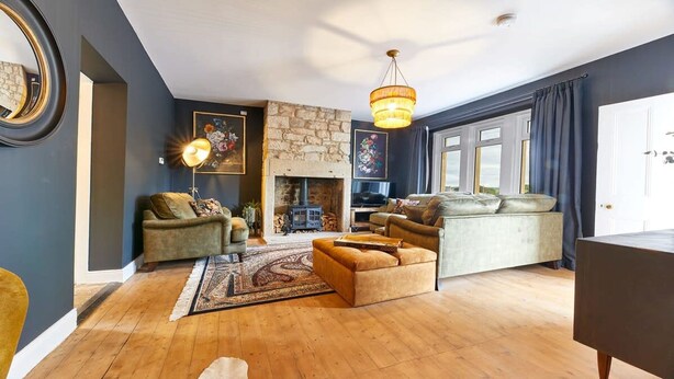 A cozy living room with a stone fireplace, a large window with curtains, and a chandelier.