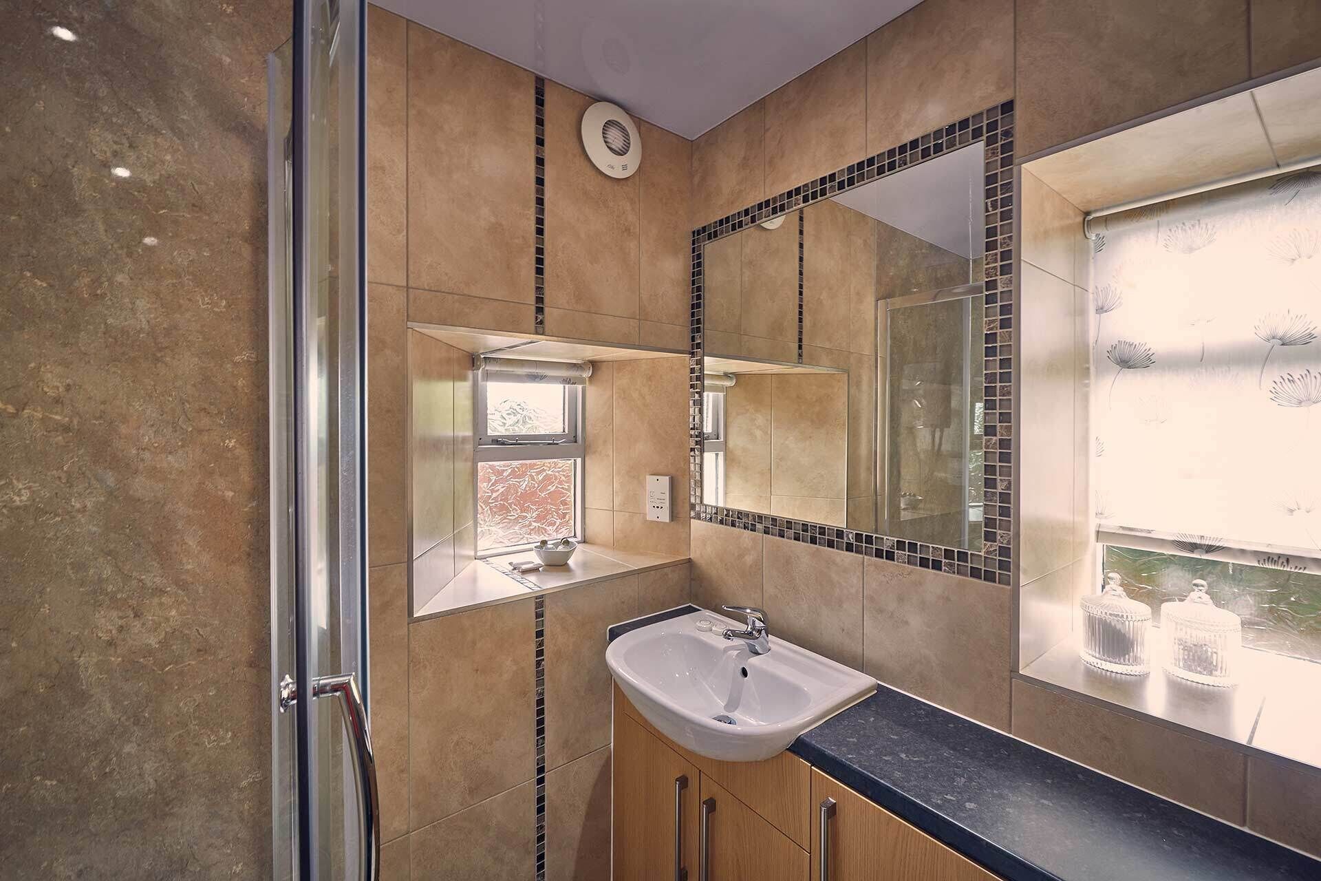 Une salle de bain avec une douche à parois de verre, un lavabo avec un miroir au-dessus et une fenêtre donnant sur l’extérieur.