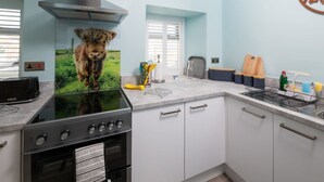 A kitchen with a stove, oven, and a wall-mounted picture of a cow. - Host Stay No 2 Lavender Cottage (Belford)