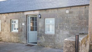 A stone building with a grey door, two windows with shutters, and a small lamp. - Host Stay No 2 Lavender Cottage (Belford)