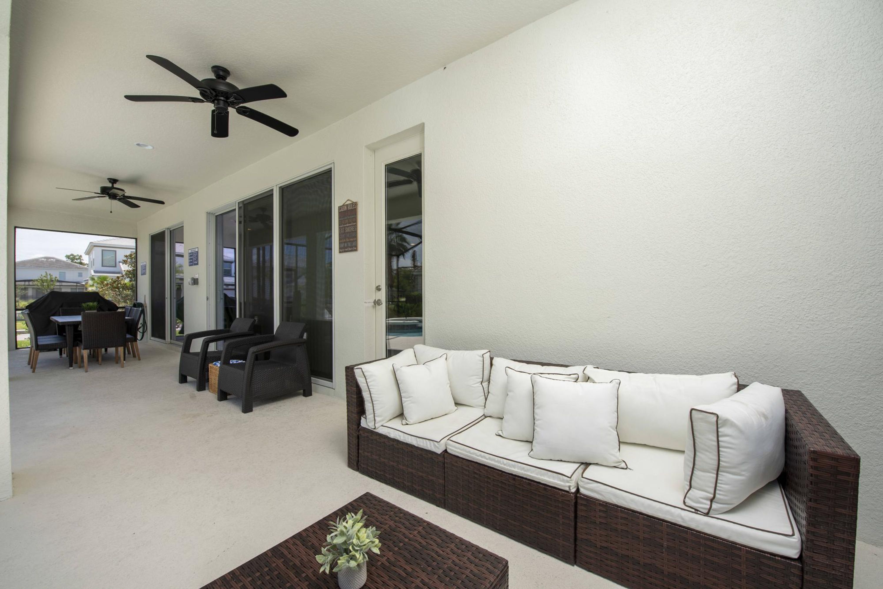 A covered patio with a sofa, chairs, a table, and ceiling fans.