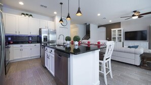 A modern kitchen with white cabinets, a central island, and pendant lighting. - Bellavida Resorts 9 Themed bd Private Pool Disney (Kissimmee)
