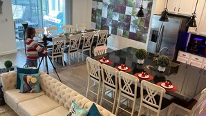 A modern living room with a beige sofa, dining area with white chairs, and a kitchen with stainless steel appliances. - Bellavida Resorts 9 Themed bd Private Pool Disney (Kissimmee)