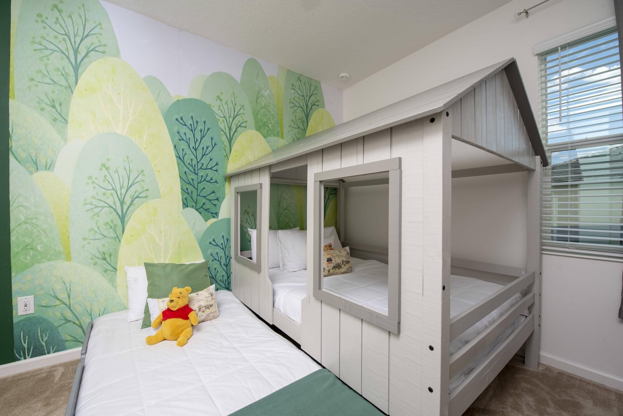 Une chambre avec des lits superposés, une fresque murale verte et un ours en peluche à l’effigie de Winnie l’ourson.