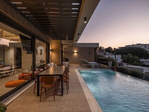 Un'area piscina moderna all'aperto con tavolo e sedie, circondata da una struttura in vetro.
