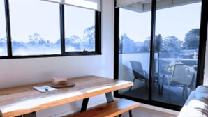 A modern room with a wooden table, a bench, and a bed. Large windows offer a view of the outdoors. - Sanctuary-Effortless City Escape (Abbotsford)