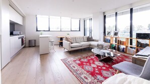 A modern living room with a white sofa, a coffee table, and a bookshelf filled with books. - Sanctuary-Effortless City Escape (Abbotsford)