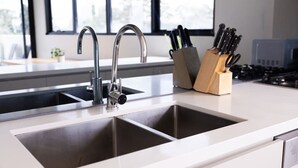 A modern kitchen with two stainless steel sinks, a knife block, and a window with a view of trees. - Sanctuary-Effortless City Escape (Abbotsford)