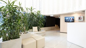 A modern reception area with a white reception desk, comfortable seating, and large potted plants. - Sanctuary-Effortless City Escape (Abbotsford)