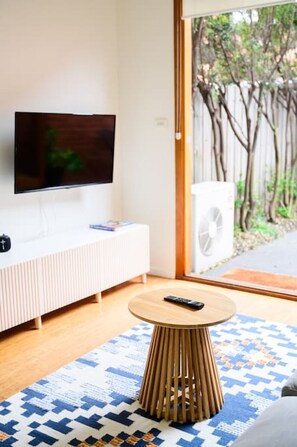 Relax in this stylish living room with a flat-screen TV, round coffee table, and large window offering a view of the outdoors.