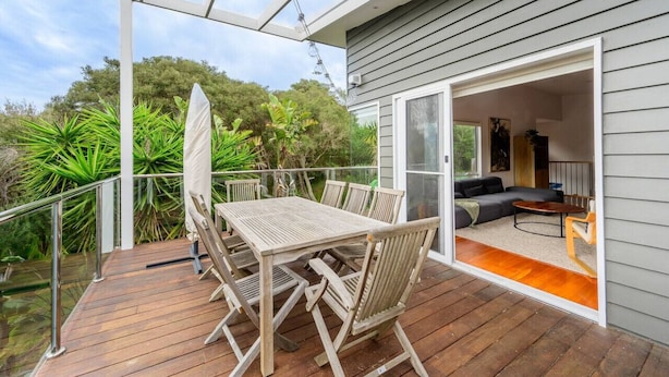 A wooden deck with a table and chairs, a glass door leading to a living area with a sofa and coffee table, and a view of greenery. - Retreat, short drive to Beach (Rye)