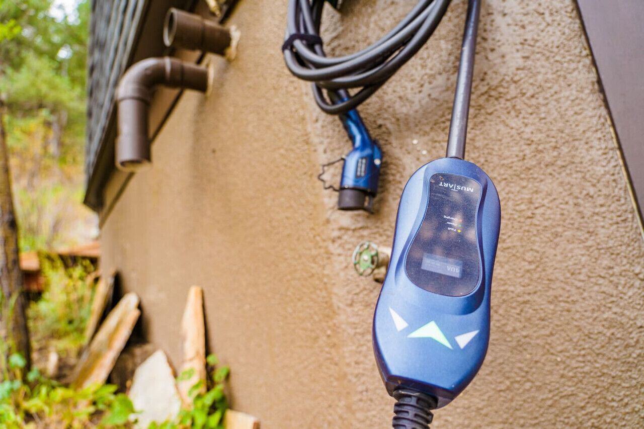 A blue power tool with a digital display, a coiled cable, and a metal pipe on a textured wall.