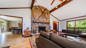 Un salón espacioso con chimenea de piedra, vigas de madera y un amplio ventanal con vistas a la vegetación.