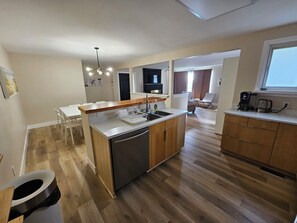 A modern kitchen with a central island, wooden cabinets, and a built-in dishwasher.