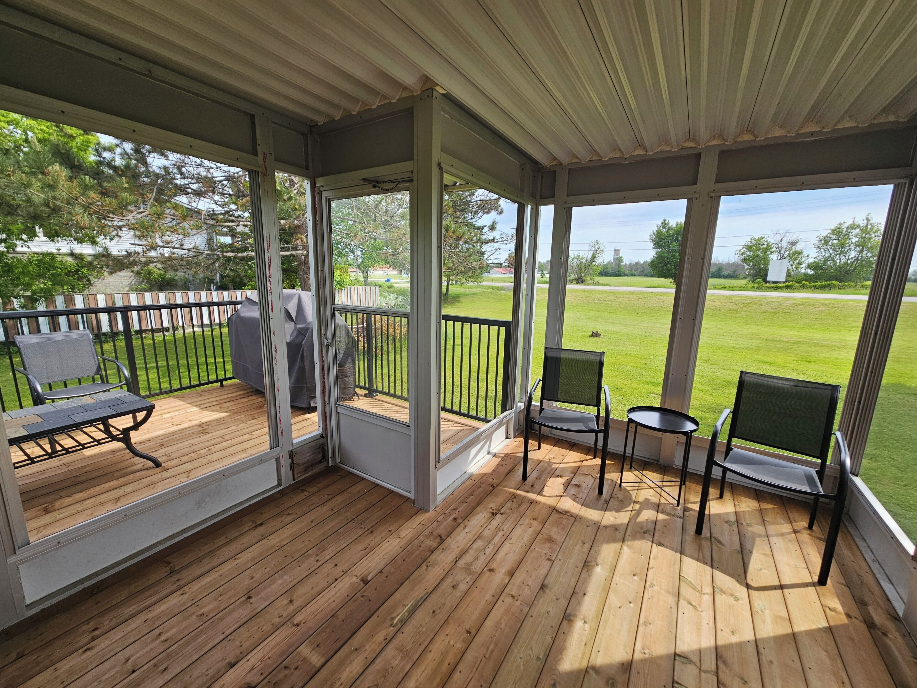 A covered deck with wooden flooring, metal railings, and two chairs.