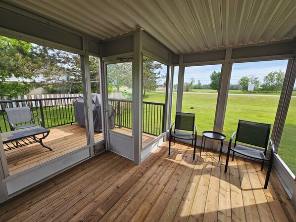 A covered deck with wooden flooring, metal railings, and two chairs.