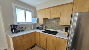 A modern kitchen with wooden cabinets, a stainless steel refrigerator, a microwave, a coffee maker, and a gas stove.