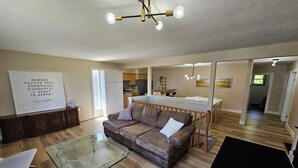 A modern living room with a glass coffee table, leather sofa, and a dining area with a kitchen in the background.