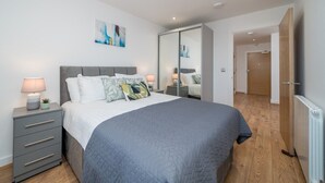Une chambre à coucher moderne avec un grand lit, des tables de chevet avec des lampes, une armoire et un tableau au mur.