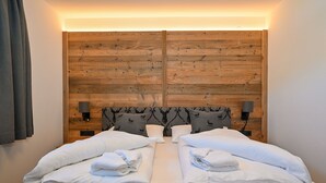 Ein Doppelbett mit weißer Bettwäsche und zwei Kissen, ein Holzkopfende mit Muster sowie zwei Wandlampen.