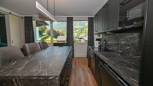 Eine moderne Küche mit Marmorarbeitsplatte, Holzboden und Blick auf eine grüne Landschaft.