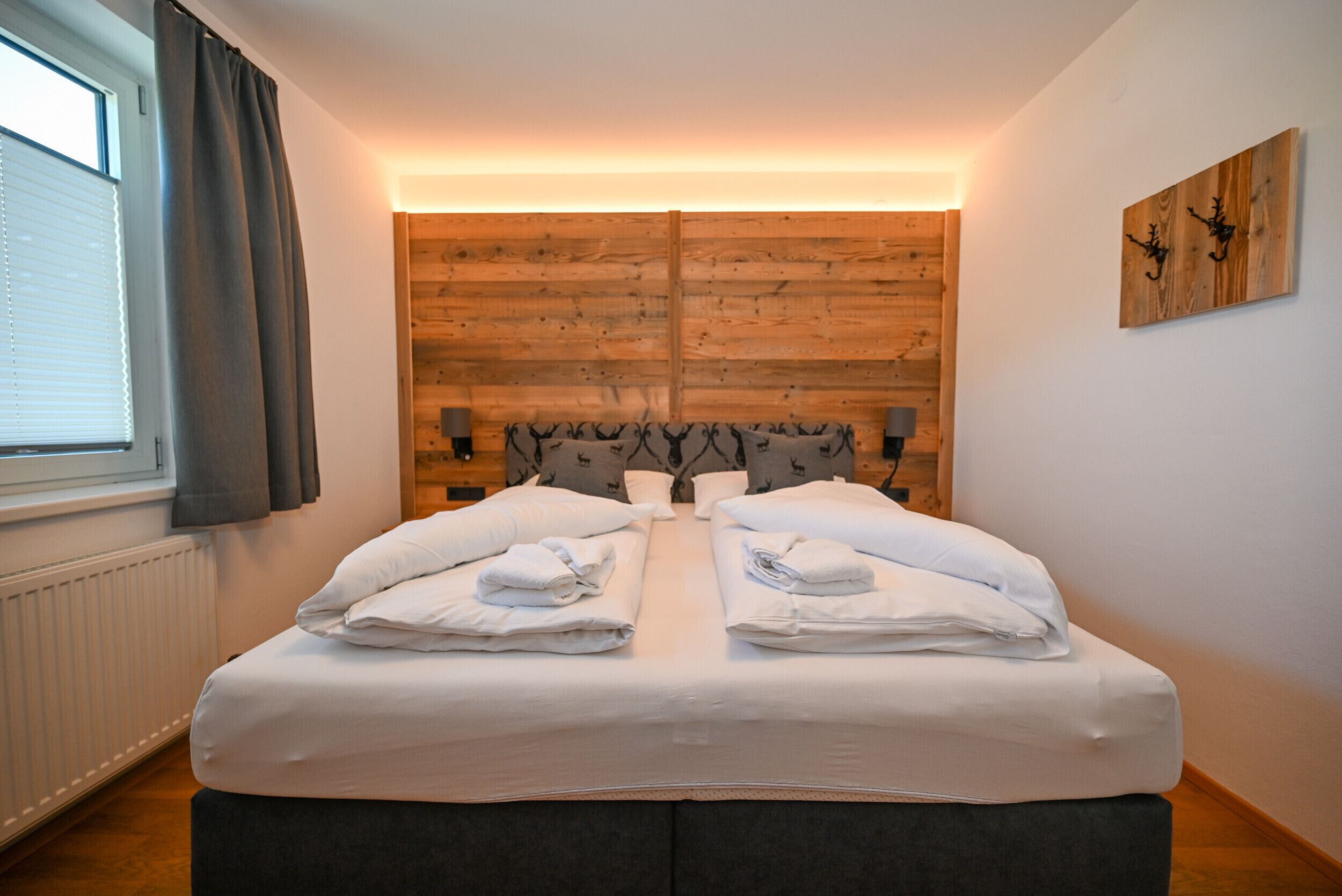 Un lit double avec des serviettes soigneusement pliées, une tête de lit en bois et une fenêtre avec des rideaux.