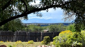 A view through a wooden fence with a rocky foreground, a wooden structure in the middle, and a distant landscape with mountains. - 2 Bedroom, 2 Bathroom Luxury Townhome; 0.3 miles to Canyon Rd;  AC; Lovely Views (Santa Fe)