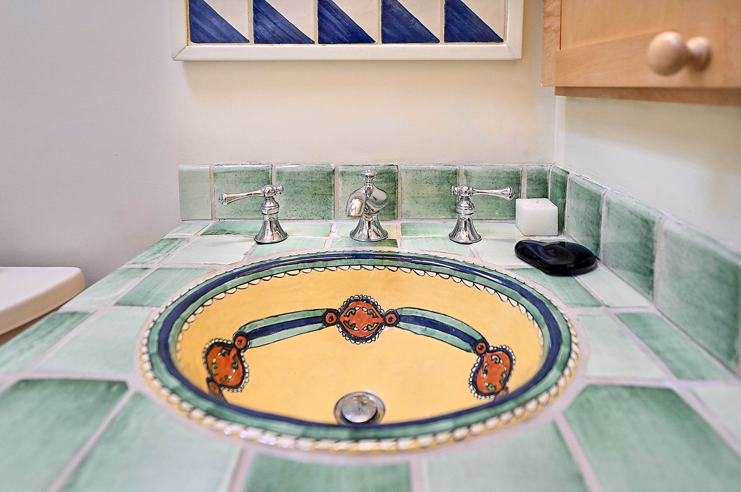 Een badkamer met een betegeld wastafelmeubel, drie kraanwerk en een zeepdispenser.
