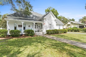 A two-story house with a front porch, a small front yard, and a driveway leading to the house.