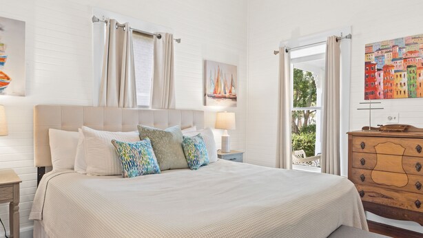 A bedroom with a large bed, a dresser, a nightstand, and a window with curtains. - Bay view Historic home walking to St. Joseph Bay and Downtown.  (Port St. Joe)
